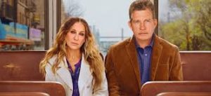 Screenshot from the HBO show "Divorce" of Sarah Jessica Parker and Thomas Haden Church sitting side by side on a bus. Parker is wearing a white jacket and purple shirt. Church is wearing a blue shirt and brown jacket. Both are looking at the camera and seem tired and slightly frustrated.