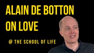 Text: Alain de Botton on love @theschooloflife. The text is bright yellow and the background is black. There is a picture of a man, Alain de Botton, in a dark collared shirt smiling and talking.
