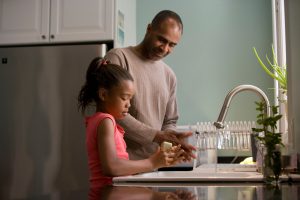 father and daughter smiling and washing dishes together