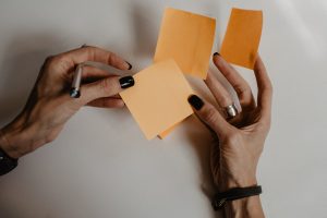 hands holding blank orange sticky notes and a pen