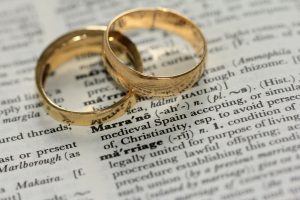 two golden marriage rings on top of a dictionary showing the word marriage