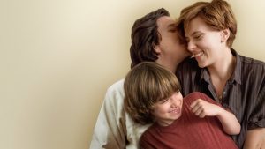 A screenshot of Adam Driver, Scarlett Johansson, and Azhy Robertson in "The Marriage Story". The three are snuggling, laughing, and smiling.